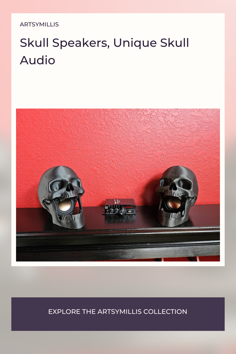 A pair of black skull speakers with open mouths, placed on a shelf in front of a red textured wall, with a small audio device
